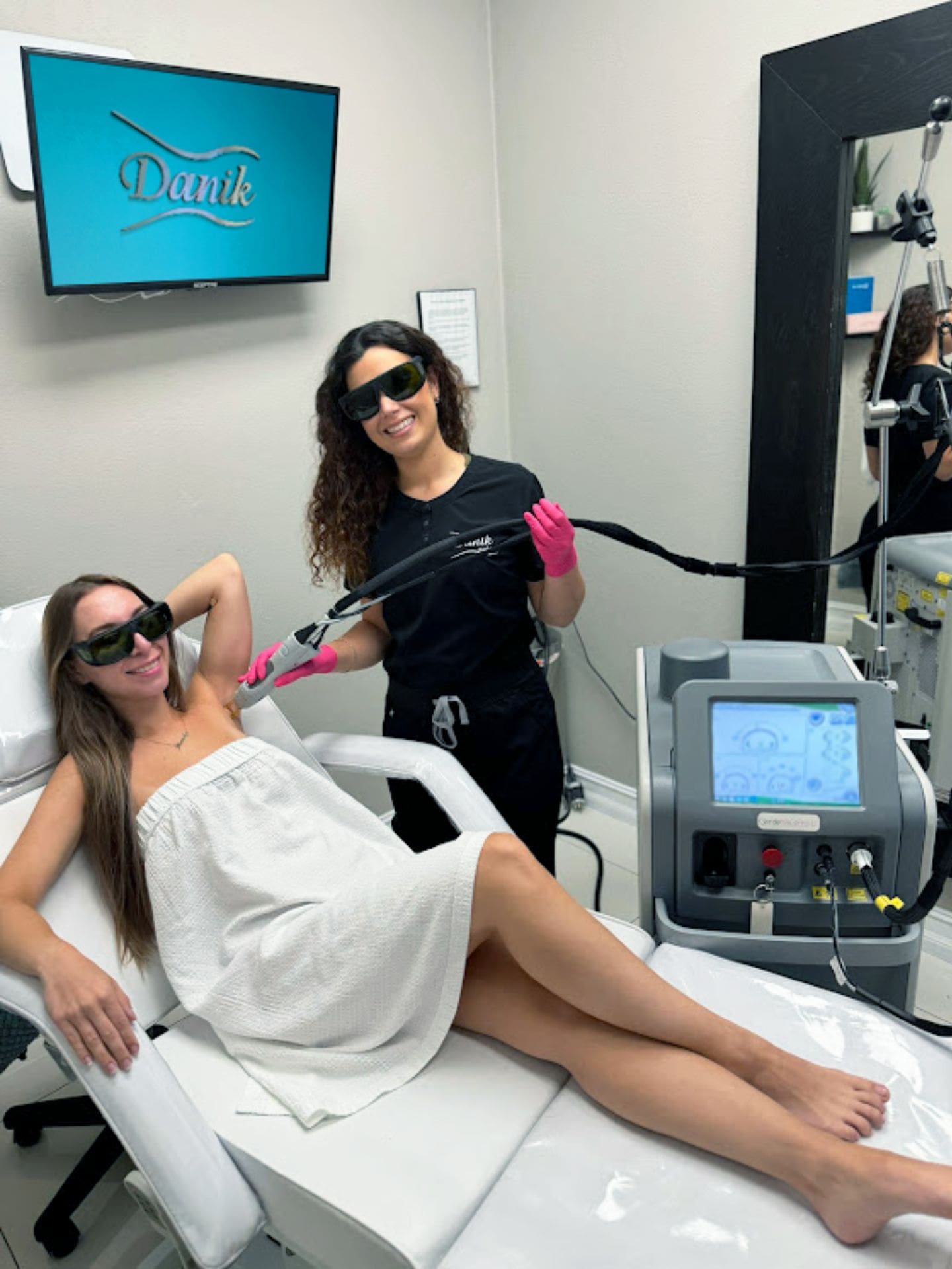 Specialist Wearing Black Uniform And Pink Gloves Applying Best Laser Hair Removal Treatment On A Woman In A White Dress Wearing Protective Glasses