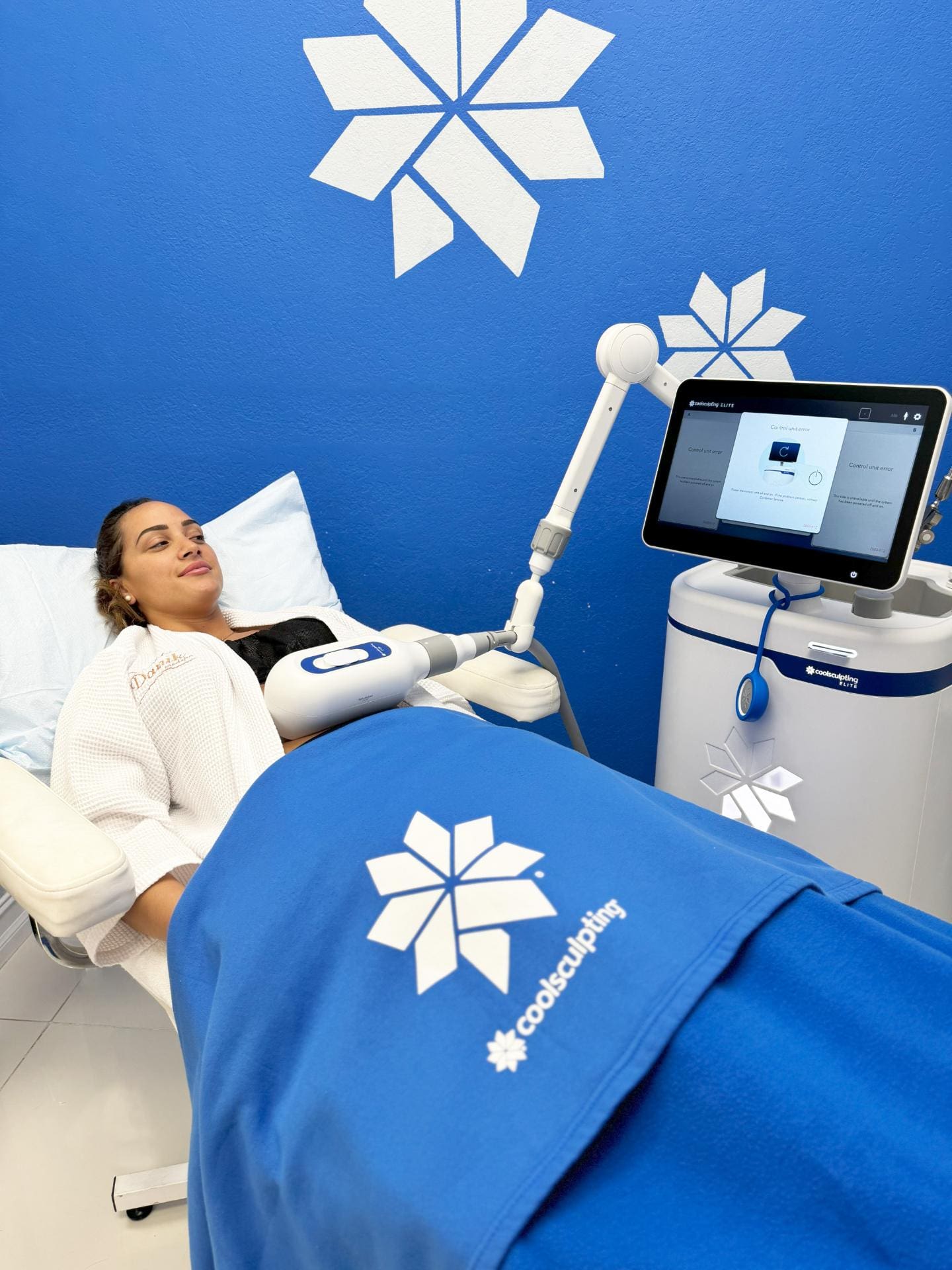 Woman Receiving CoolSculpting Treatment Laying On A Bed With A Blue CoolSculpting Blanket On Her And A Monitor To Her Right