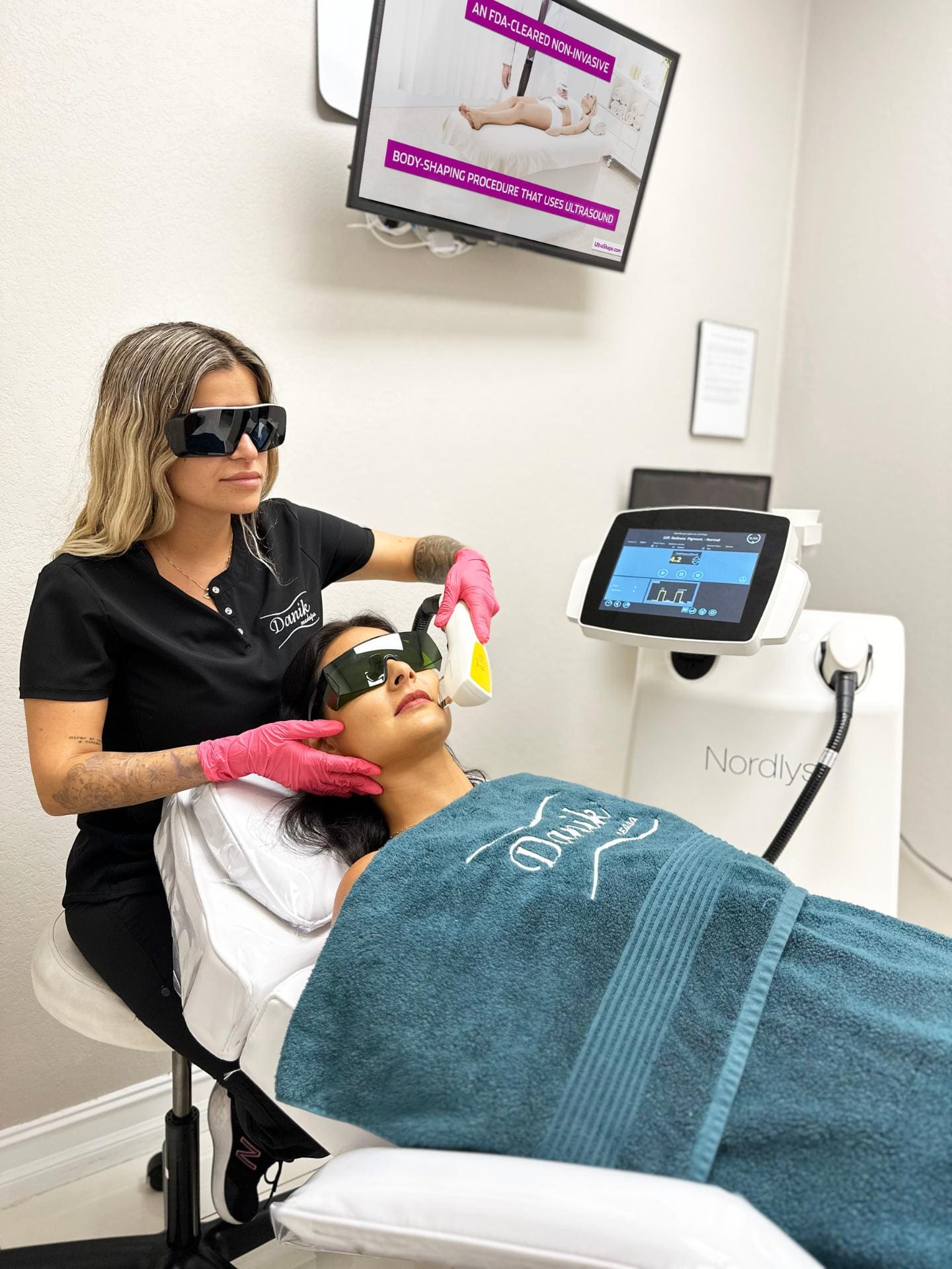 Specialist Wearing Black Uniform And Protective Glasses Applies IPL Facial Rejuvenation Treatment To A Woman In A Blue Towel And Protective Glasses