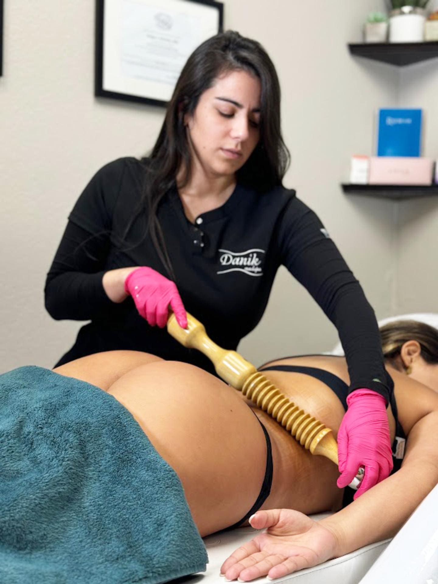 Woman Receiving Wood Therapy Body Sculpting Treatment On Her Back From A Specialist In Black Uniform And Pink Gloves